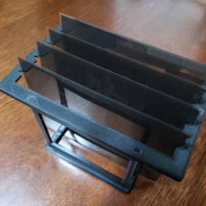 May include: A black plastic frame with four clear plastic slides inside. The frame is designed to hold and display photographic negatives.