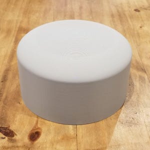 Peut inclure: Objet cylindrique gris clair avec un dessus plat et une surface texturée. Le dessus présente des rainures circulaires concentriques. Posé sur une surface en bois.