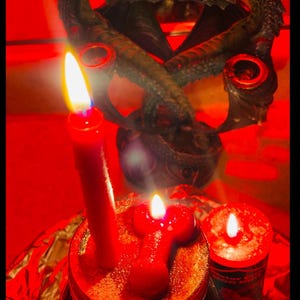 May include: Image of three lit red candles, one tall and two shorter, atop a jar. The text "POWERFUL CONJURE JARS" is at the top. The background features a dark, ornate sculpture. The scene is bathed in red light.