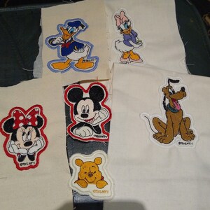 May include: Embroidered patches of Disney characters including Donald Duck, Daisy Duck, Minnie Mouse, Mickey Mouse, Winnie the Pooh, and Pluto. Each patch is on white fabric with colourful stitching and the Disney logo.