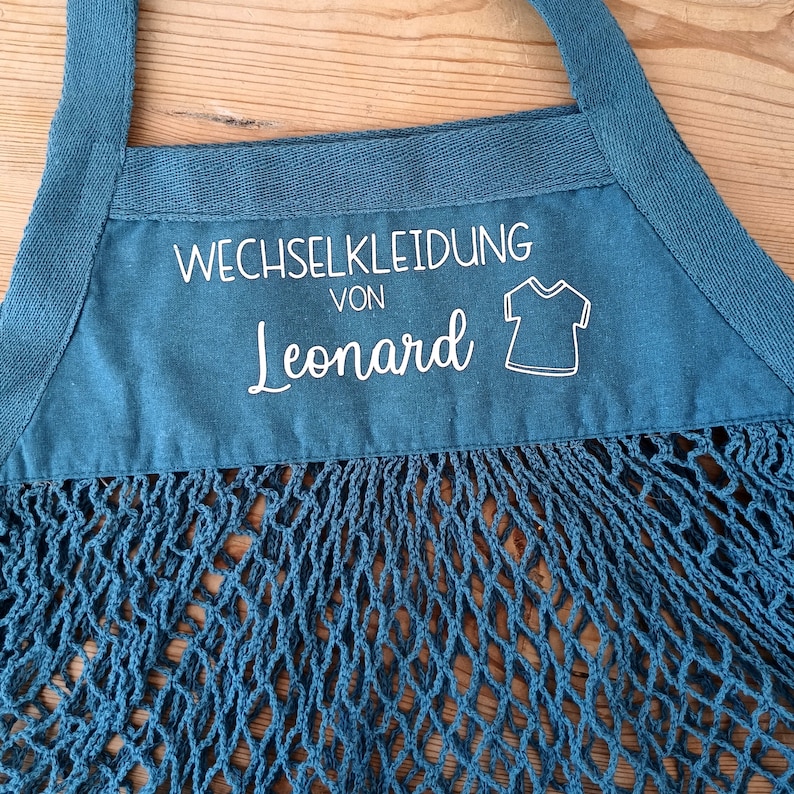 May include: A blue mesh bag with a white label that says "Wechselkleidung von Leonard" and a small graphic of a t-shirt.