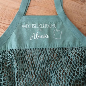 May include: A green mesh bag with a white label that says "Wechselkleidung von Alexia" and a small white outline of a t-shirt.