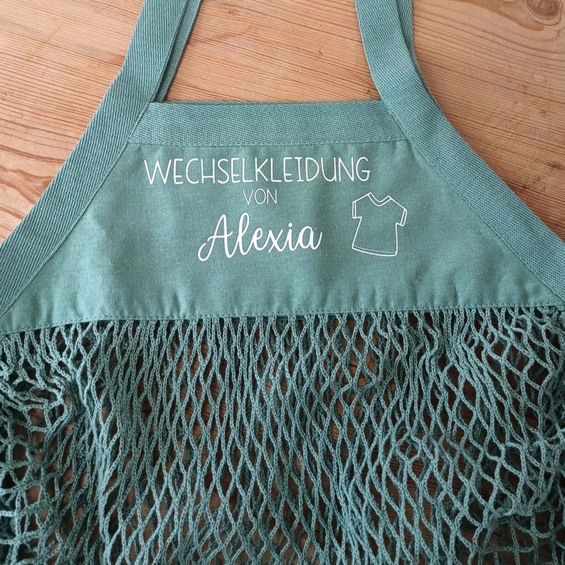 May include: A green mesh bag with a white label that says "Wechselkleidung von Alexia" and a small white outline of a t-shirt.