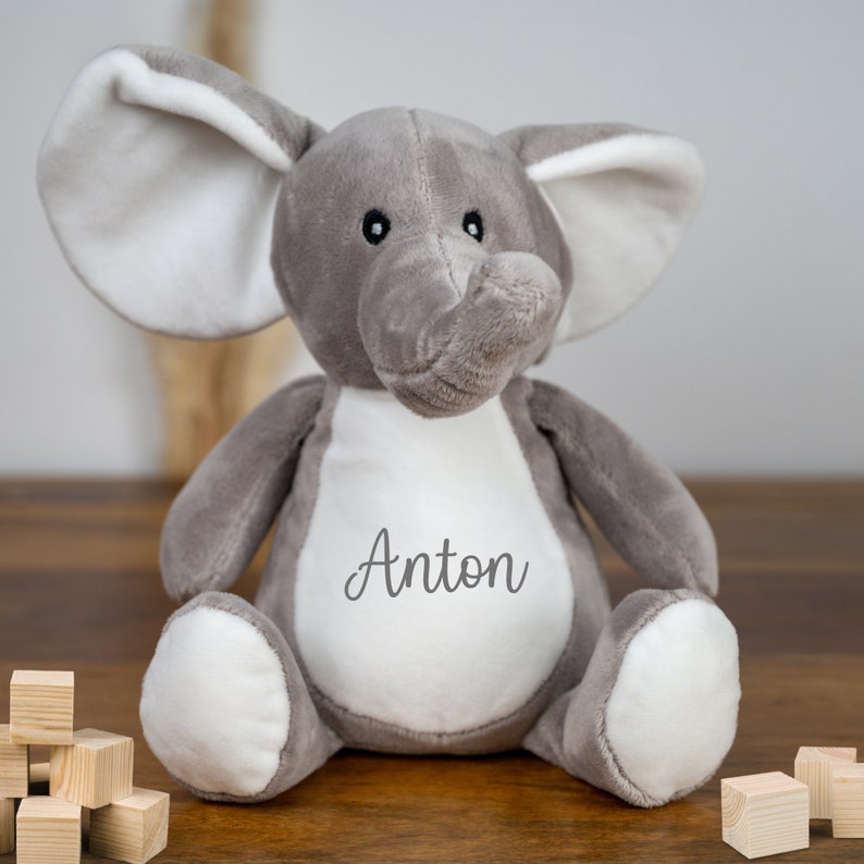 May include: A gray and white plush elephant toy with a white patch on its chest that says "Anton".