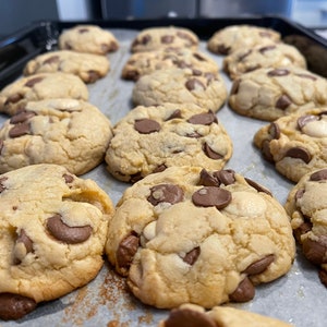 Può includere: Una teglia da forno piena di biscotti con gocce di cioccolato appena sfornati. I biscotti sono dorati e hanno una varietà di gocce di cioccolato sulla parte superiore.