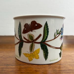 May include: White ceramic mug with a floral design featuring butterflies, leaves, and flowers. The mug has the text "Speedwell" on the bottom.