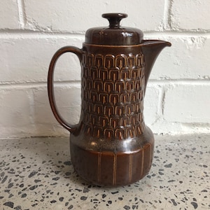 May include: A brown ceramic coffee pot with a geometric pattern. The pot has a lid and a handle.