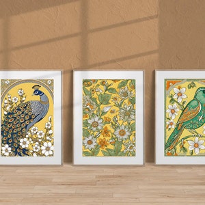 May include: Three framed prints with yellow backgrounds and floral designs. The left print features a blue peacock with a spread tail. The center print features white flowers and green leaves. The right print features a green bird with a white flower in its beak.