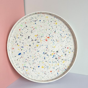 May include: A white round tray with a speckled terrazzo design featuring blue, red, yellow, and green flecks.