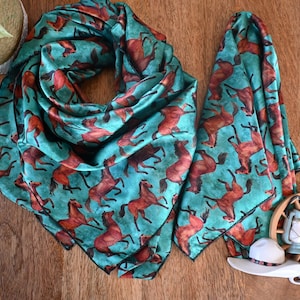 May include: Two turquoise blue silk bandanas with a brown horse print. The bandanas are folded and laid out on a wooden surface.