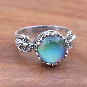 May include: A silver ring with a large, round, color-changing stone. The stone shifts from blue to green to purple. The ring has decorative floral accents on the sides and the text "AS Sellers Store".