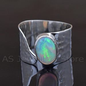 May include: A silver ring with a large, oval opal gemstone. The opal displays a play of color with green and blue hues. The ring has a textured band and a modern, open design. The text "AS Jewellers Store" is visible.