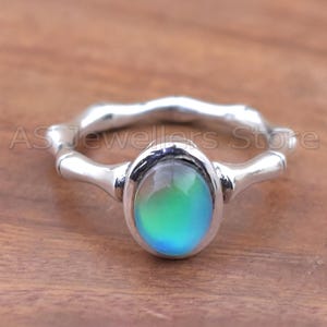 May include: A silver ring with an oval, color-changing stone. The stone shifts from green to blue. The ring band has a textured, organic design. The text "AS Jewellers Store" is visible on the ring.