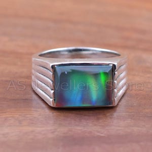 May include: A silver ring with a rectangular black opal gemstone. The opal displays a play of color with green, blue, and red hues. The ring band has a ridged design. The text "AS Jewellers Store" is visible.