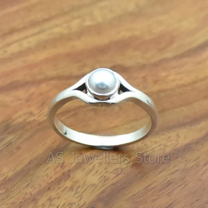 K&ouml;nnte beinhalten: Ein silberner Ring mit einem wei&szlig;en Perlmutt, das in einem schlichten, eleganten Design gefasst ist.