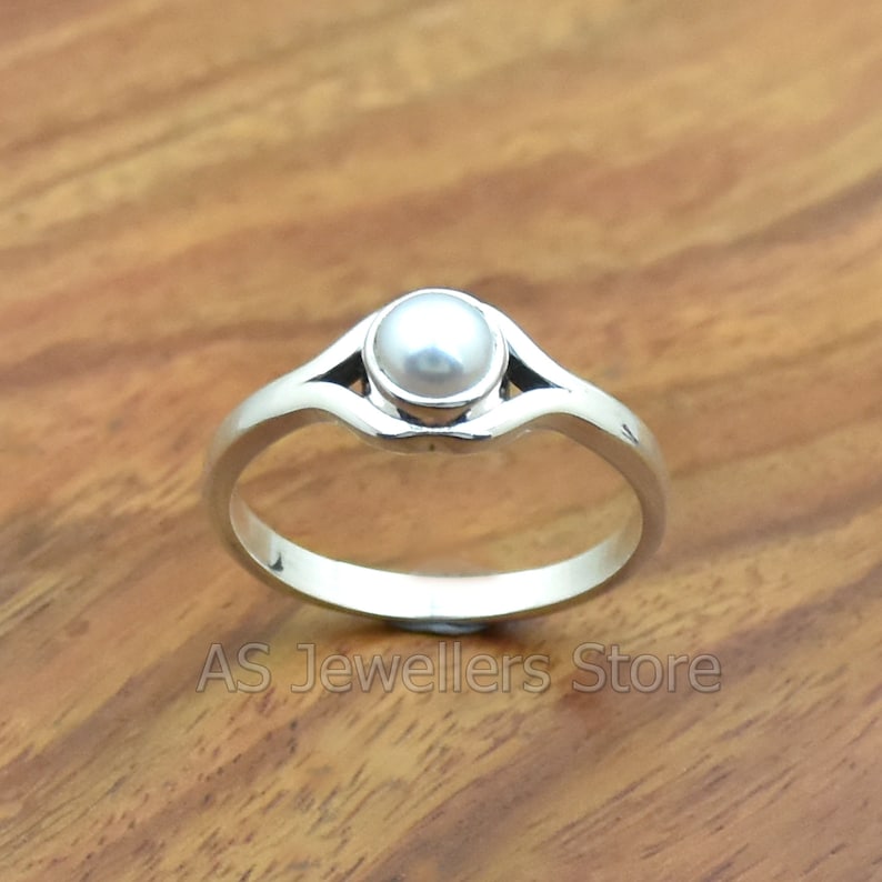 K&ouml;nnte beinhalten: Ein silberner Ring mit einem wei&szlig;en Perlmutt, das in einem schlichten, eleganten Design gefasst ist.