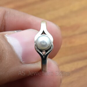K&ouml;nnte beinhalten: Ein silberner Ring mit einem wei&szlig;en Perlmutt, das in einem filigranen, durchbrochenen Design eingefasst ist.