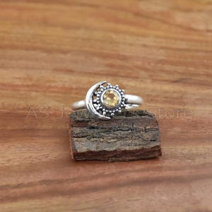 May include: A silver ring with a crescent moon design and a yellow gemstone in the center.