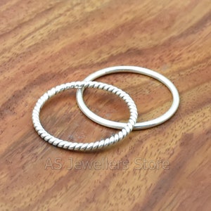 May include: Two silver rings, one with a twisted design and the other plain, on a wooden surface.