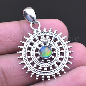 May include: A silver pendant with a sunburst design. The pendant features a central, iridescent gemstone surrounded by concentric circles and beaded edges. The pendant has a loop for a chain.