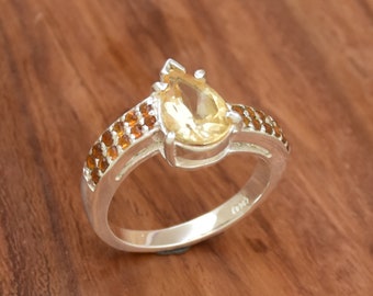 May include: A silver ring with a pear-shaped yellow gemstone and a band of smaller brown gemstones.