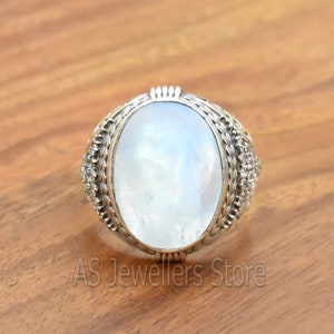 May include: A silver ring with a large oval moonstone set in a detailed silver band. The band is decorated with small silver beads and a rope-like design.