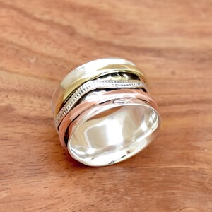 Può includere: Un anello rotante in argento, oro e rame. L'anello è composto da tre bande che ruotano l'una intorno all'altra. L'anello è una scelta popolare per la meditazione e la consapevolezza.