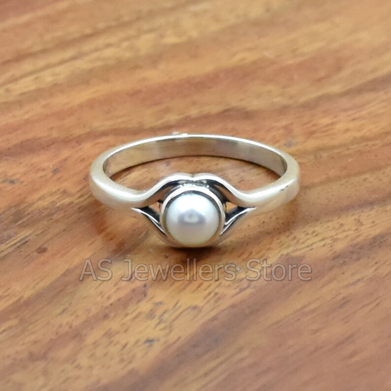 K&ouml;nnte beinhalten: Ein silberner Ring mit einem wei&szlig;en Perlmutt, das in einem zarten, geschwungenen Design gefasst ist.
