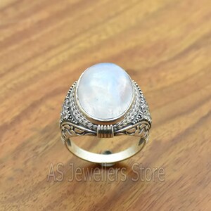 May include: A silver ring with a large oval moonstone set in a detailed floral design.