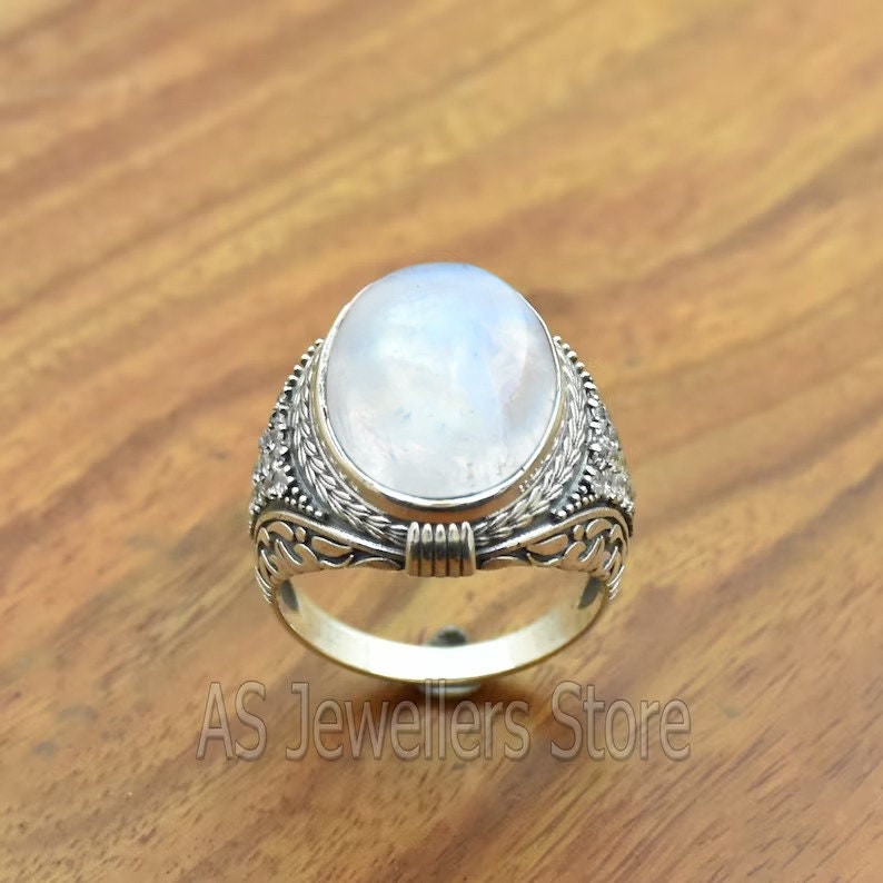 May include: A silver ring with a large oval moonstone set in a detailed floral design.