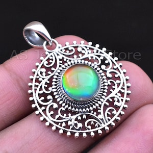 May include: A silver pendant with a round, iridescent gemstone at the center. The gemstone displays a spectrum of colors. The pendant has an ornate, openwork design around the stone, with the text "AS J store" visible.