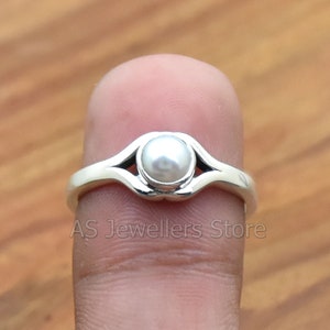 K&ouml;nnte beinhalten: Ein silberner Ring mit einem wei&szlig;en Perlmutt, das in einem zarten, offenen Design gefasst ist.