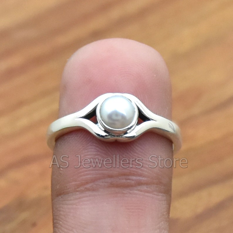 K&ouml;nnte beinhalten: Ein silberner Ring mit einem wei&szlig;en Perlmutt, das in einem zarten, offenen Design gefasst ist.