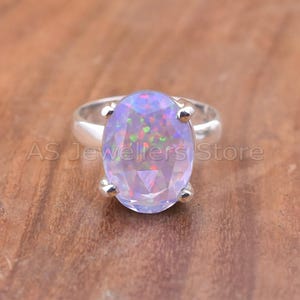 May include: A silver ring featuring a large, oval-cut opal gemstone. The opal displays a play of color with flashes of blue, green, and red. The ring's band is smooth and polished, and the gemstone is held in place by four prongs.