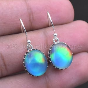 May include: A pair of silver drop earrings with oval, iridescent stones. The stones display a spectrum of colors, including blue, green, and yellow. The earrings have a decorative silver setting and a simple hook closure. The text "AS Jewellers Store" is visible.