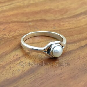 K&ouml;nnte beinhalten: Ein silberner Ring mit einem wei&szlig;en Perlmutt, das in einem filigranen, durchbrochenen Design gefasst ist.