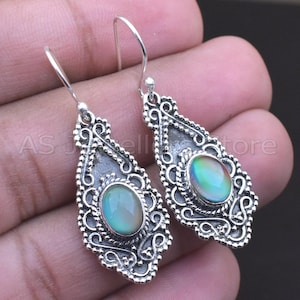 May include: A pair of silver-toned dangle earrings. Each earring features an oval, iridescent stone set within an ornate, filigree-style frame. The earrings have a hook closure.