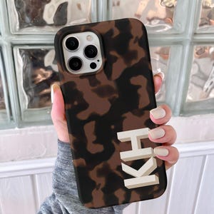 May include: A brown and black tortoiseshell phone case with the letters "KH" in white on the back.