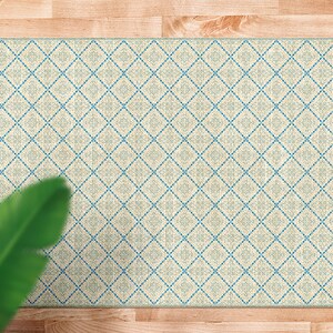 Op de afbeelding: Een crèmekleurig tapijt met een geometrisch patroon in blauw en wit. Het tapijt heeft een ruitpatroon met een klein bloemachtig ontwerp in elke ruit.