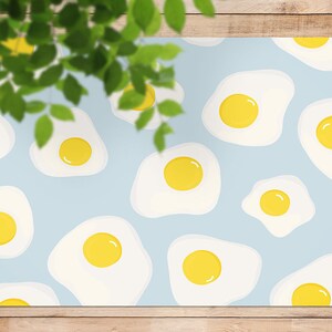 Può includere: Uno sfondo azzurro è ricoperto da un motivo di uova fritte. Ogni uovo ha un tuorlo giallo e un albume bianco. Le foglie verdi oscurano parzialmente l'immagine nell'angolo in alto a sinistra.