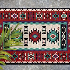 Può includere: Un tappeto colorato con un motivo geometrico in tonalità di rosso, verde, nero e bianco. Il tappeto ha un design tradizionale con un motivo centrale e un bordo.