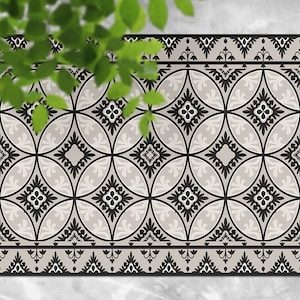 Può includere: Tappetino da pavimento a motivi bianco e nero con un design geometrico. Il tappetino ha un bordo con un motivo ripetitivo di fiori stilizzati.