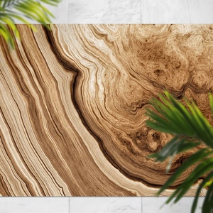 Può includere: Un tappeto rettangolare con un motivo a venature del legno nei toni del marrone e del beige. Il design presenta cerchi concentrici e motivi lineari, creando un'estetica naturale e organica. Foglie verdi in primo piano.