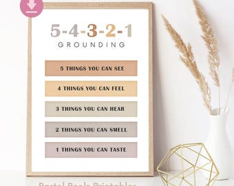 May include: A framed print with the text "5-4-3-2-1 GROUNDING" and prompts for sensory awareness. The print has a light wood frame and features pastel-colored blocks with prompts like "5 THINGS YOU CAN SEE." Decorative elements include dried plants in a white vase and a gold geometric sculpture.