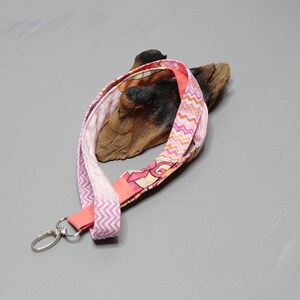 Könnte beinhalten: Ein pinkfarbenes und orangefarbenes Lanyard mit Zickzackmuster und einem silbernen Clip.