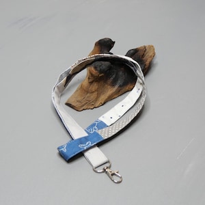 Könnte beinhalten: Ein weißes und blaues gemustertes Lanyard mit einem silbernen Schlüsselring. Das Lanyard ist aus Stoff und hat einen weißen Hintergrund mit blauen und grauen geometrischen Mustern.