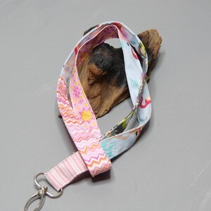 Könnte beinhalten: Ein pinkfarbenes und blaues Lanyard mit einem silbernen Drehverschluss. Das Lanyard ist aus Stoff und hat ein florales und geometrisches Muster.