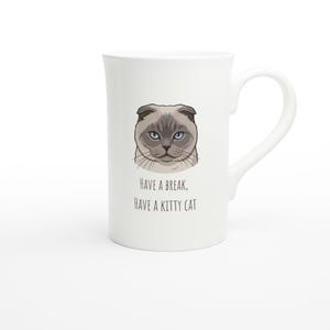 Puede incluir: Taza de cerámica blanca con una ilustración de dibujos animados de un gato gris con ojos azules. La taza tiene el texto "HAVE A BREAK, HAVE A KITTY CAT" impreso debajo de la imagen del gato. La taza tiene un asa curva.