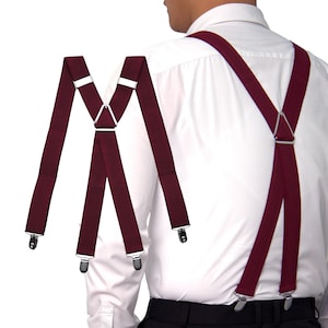 May include: Burgundy suspenders with silver metal clips and adjusters. The suspenders are shown against a white shirt and black trousers. The suspenders are an X-back style, with a metal triangle connecting the straps at the back.