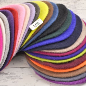 May include: A stack of 20 colourful felt berets in various shades of pink, purple, blue, green, brown, orange, and yellow. The berets are arranged in a semi-circle with the label "BASIC SENSE" visible on the top beret.